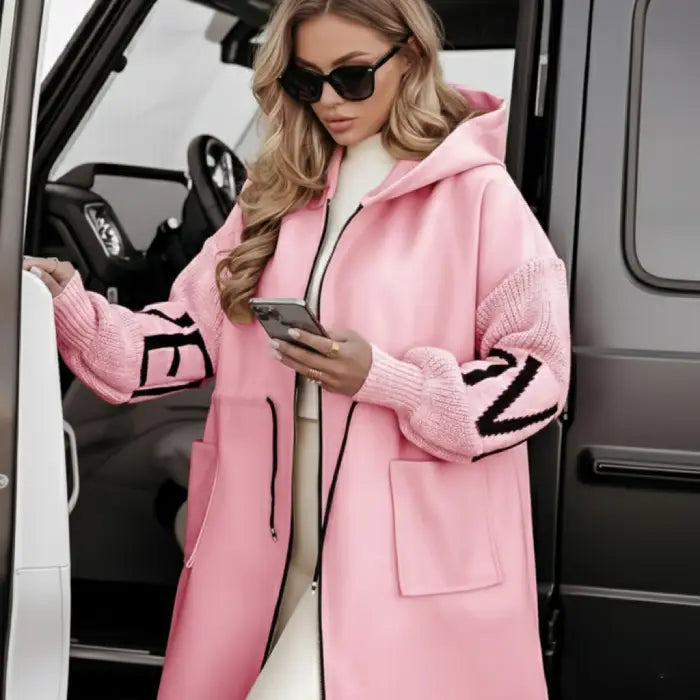 Women’s long hooded cardigan coat in soft pink paired with neutral outfit near car, cozy knit design offering chic comfort for modern style
