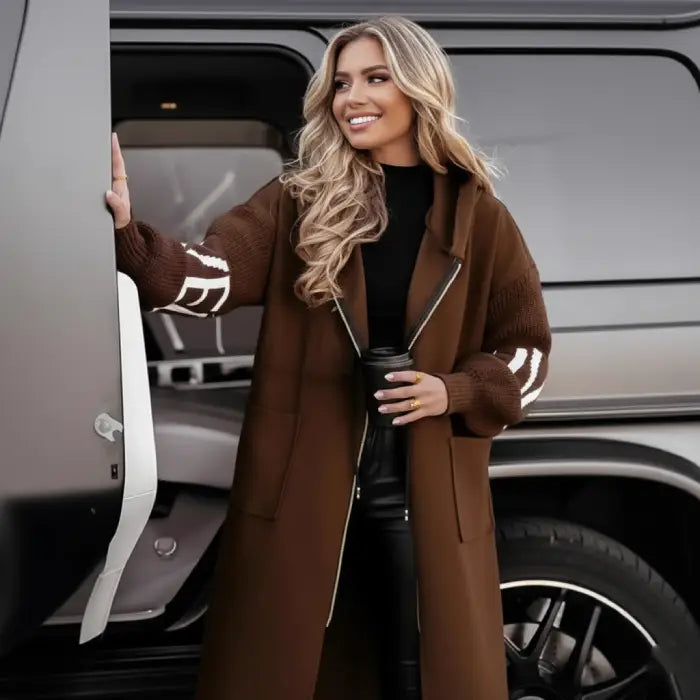 Women’s long hooded cardigan coat in rich brown worn beside vehicle, cozy knit sleeves adding warm luxury style for modern fall outfits