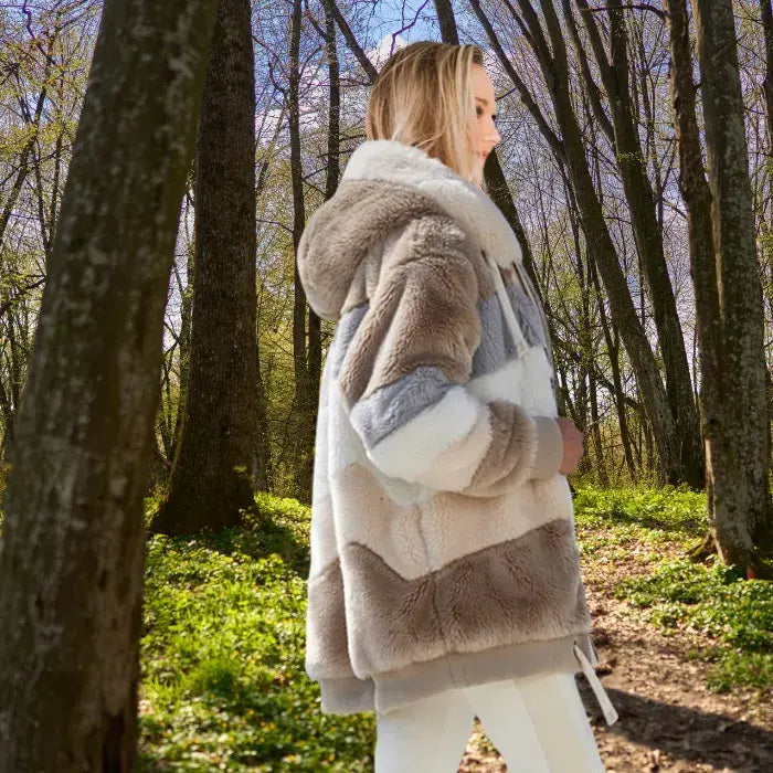 Womens loose plush coat in beige and gray tones worn in a forest path.