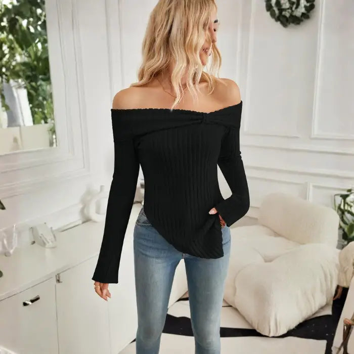Side angle of women's off shoulder black knit top featuring long sleeves and diagonal hem.