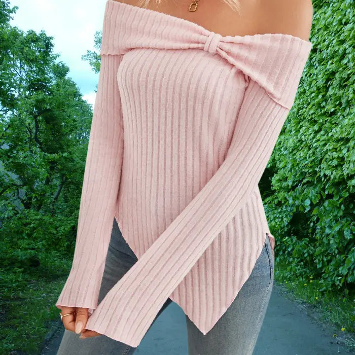 Person wearing a pink ribbed sweater with a bow detail outdoors.