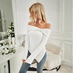 Women's off shoulder white knit top styled in elegant room with flowers and neutral decor.