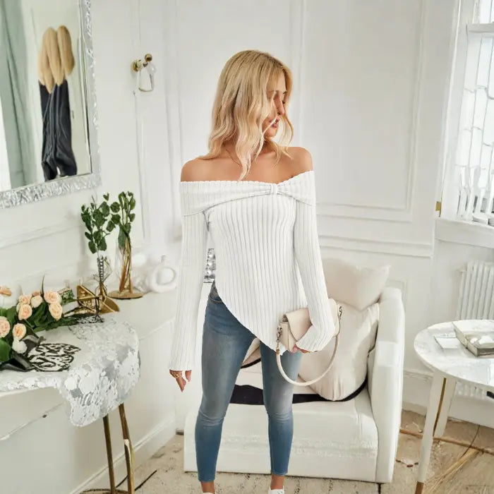 Women's off shoulder knit top in white styled with crossbody bag and indoor decor background.