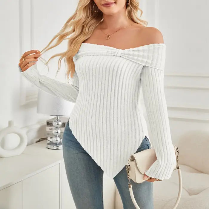 Model smiling in white off shoulder knit top with long sleeves and knot front, paired with bag.