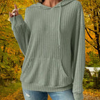 Women's Ribbed Hoodie in sage green with drawstring and front pocket, styled outdoors in autumn woods.