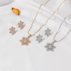 Women’s snowflake necklace and earring set in gold and silver tones displayed on silk fabric with crystal detailing for winter gift jewelry