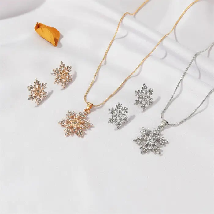 Women’s snowflake necklace and earring set in gold and silver tones displayed on silk fabric with crystal detailing for winter gift jewelry
