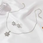 Women’s snowflake necklace and earring set in silver displayed on white background with shimmering crystal snowflakes for winter jewelry