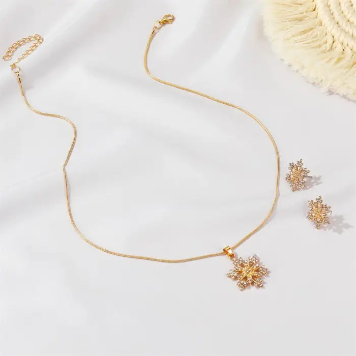 Women’s snowflake necklace and earring set in gold displayed on white fabric, featuring sparkling crystal snowflake pendant and studs