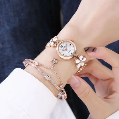 Women's watch bracelet set with white flower design worn on the wrist.