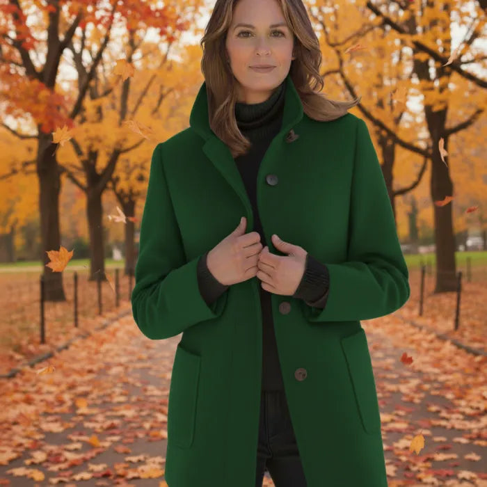 Wool pea coat in forest green worn by a woman walking through an autumn park with falling leaves.
