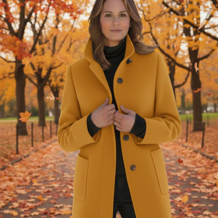 Wool pea coat in mustard yellow worn by a woman standing in a fall park with colorful leaves.