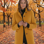 Wool pea coat in mustard yellow worn by a woman standing in a fall park with colorful leaves.