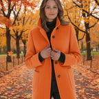 Wool pea coat in bright orange worn by a woman in an autumn park with falling leaves.