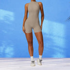 workout romper in neutral beige with front zipper and mock neck design against bright blue background for versatile fitness wear
