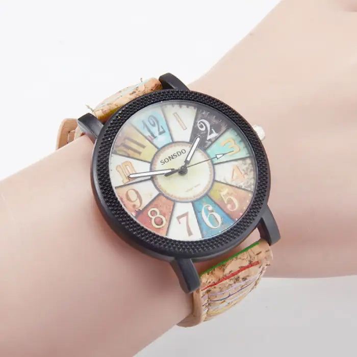 Close-up of an analog wristwatch with a cork strap and colorful vintage dial, worn on a mannequin's wrist.