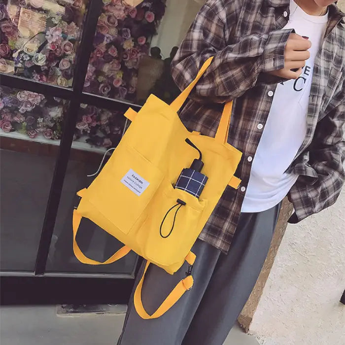 Yellow canvas tote bag with multiple compartments worn with casual plaid outfit