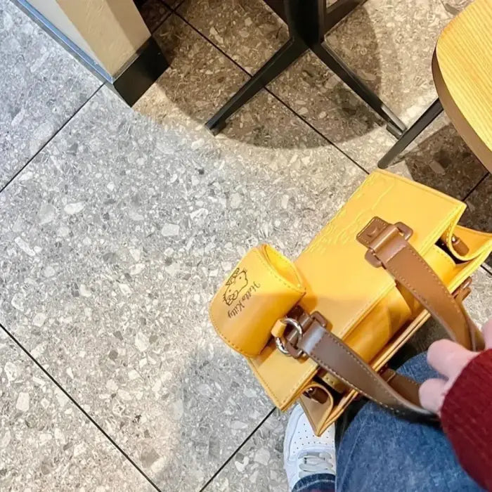 Yellow Hello Kitty handbag with brown straps placed on a table, perfect accessory for casual outings.