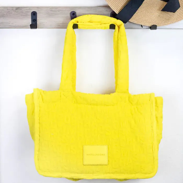 Yellow Marc Jacobs tote bag hanging on hook, displaying its vibrant color and embossed logo design.