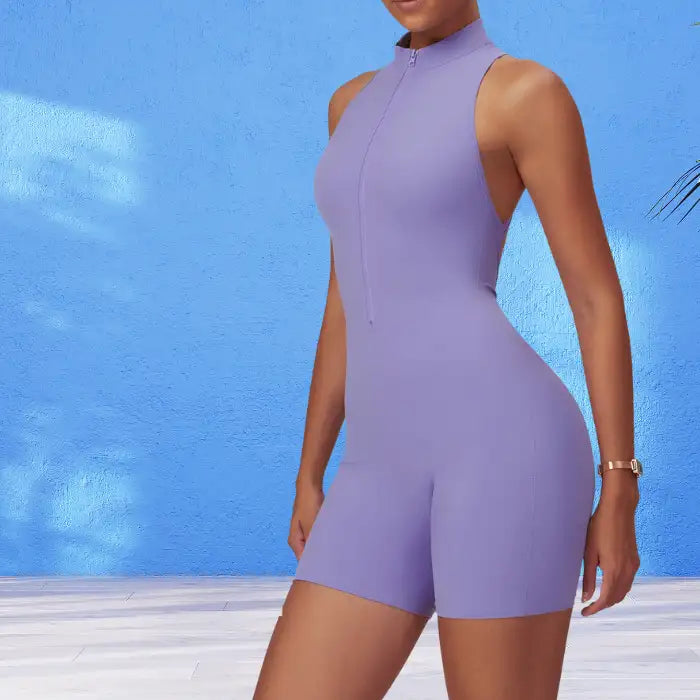 yoga bodysuit in soft lavender with zip front design against bright blue wall highlighting its sleeveless silhouette