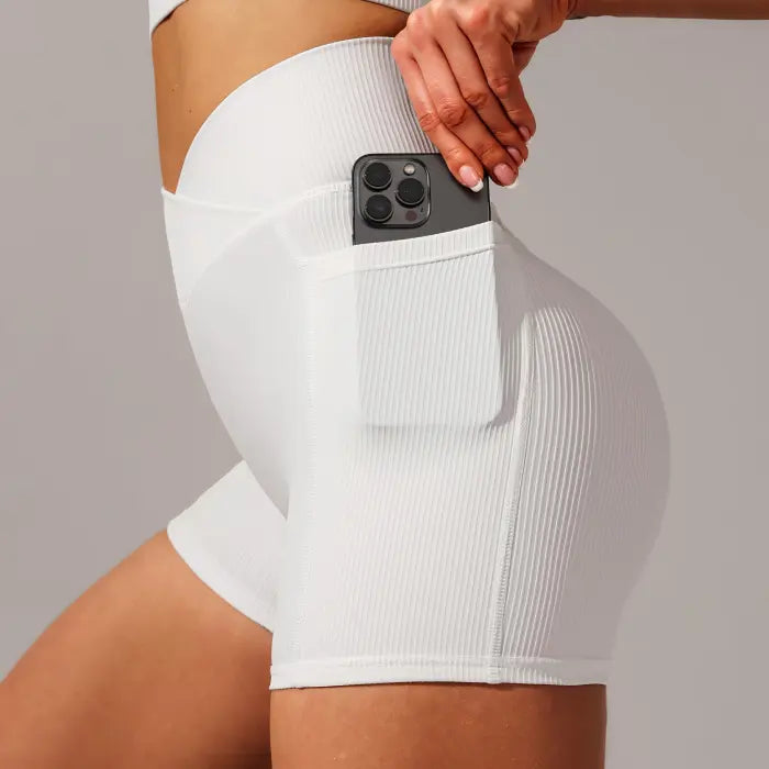 Yoga shorts set in white ribbed fabric with side pocket holding phone for hands-free workouts.