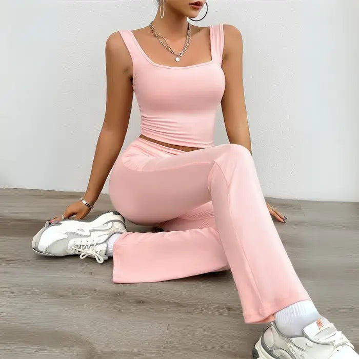 Woman in a pink yoga two-piece set sitting on the floor, wearing a trendy sleeveless crop top and flared pants.

