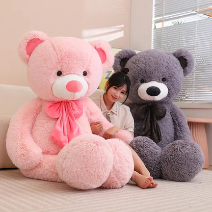 Brown teddy bear with a soft bow sitting in the corner of a cozy room.